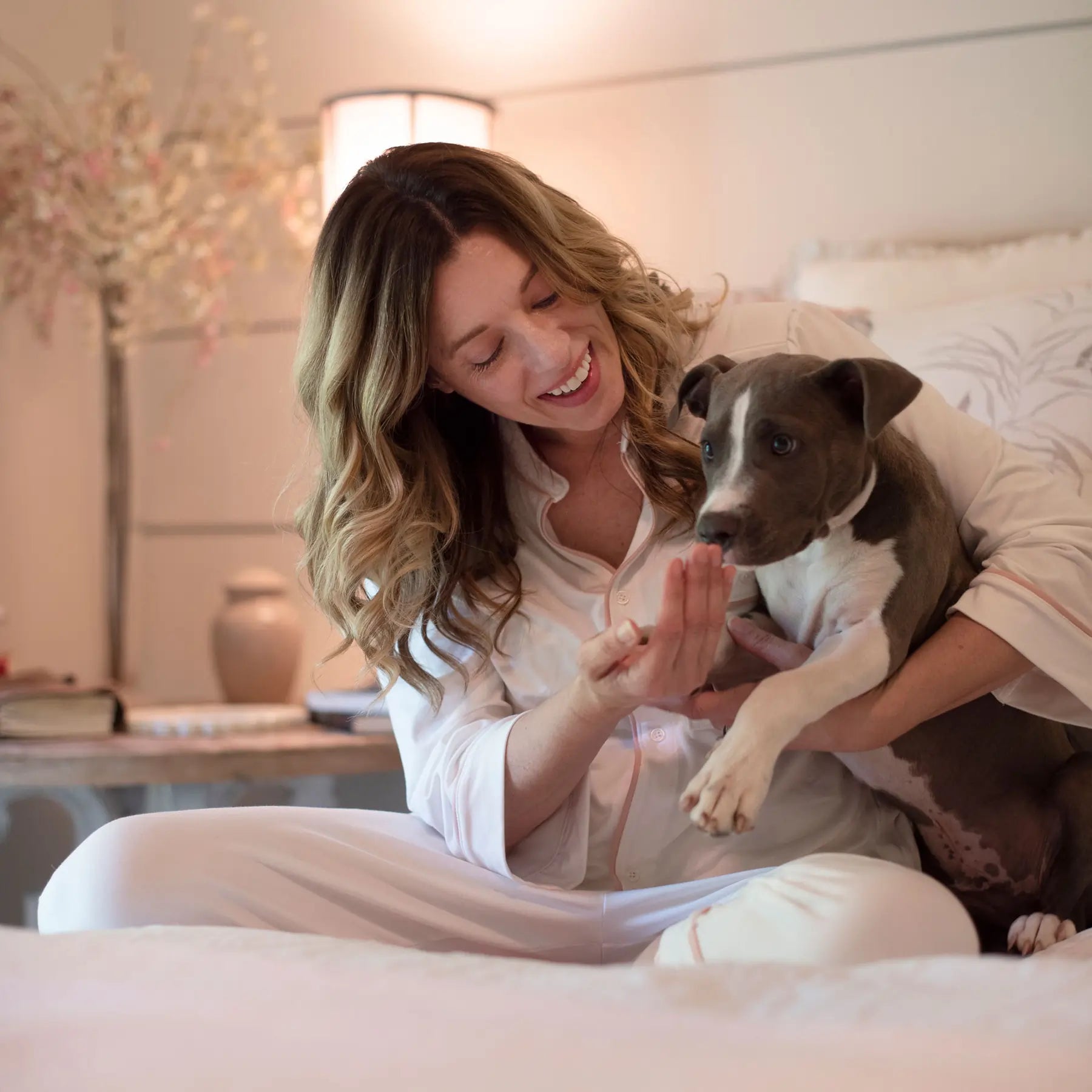A woman wearing Just Because Love Does medically mindful pajamas on her bed with her dog.